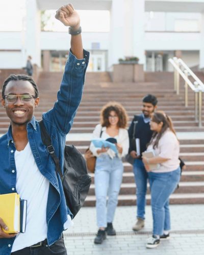 Joyful african american student celebrating success and education, holding books with diverse friends on university campus